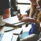 crowd gathers near laptop over coffee business plan meeting