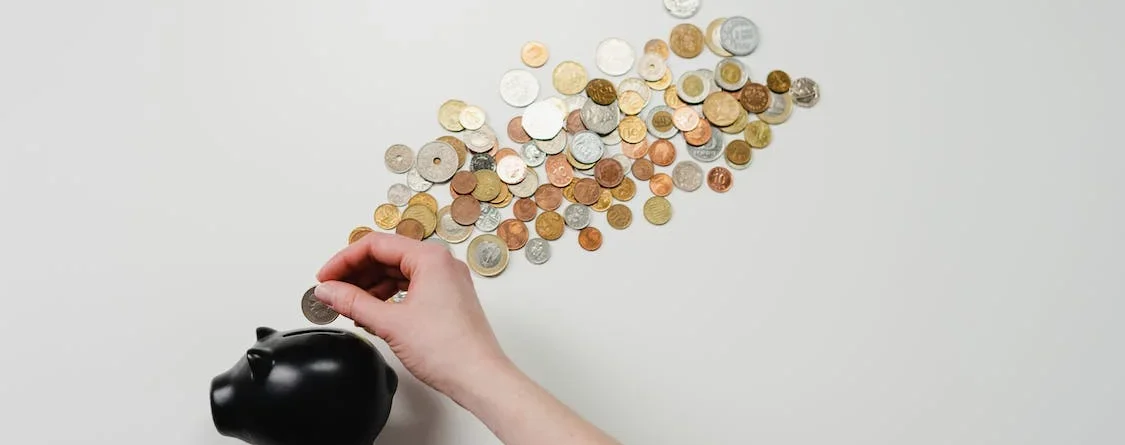 hand putting coins in a black coated piggy bank with coins scattered behind it