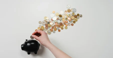 hand putting coins in a black coated piggy bank with coins scattered behind it